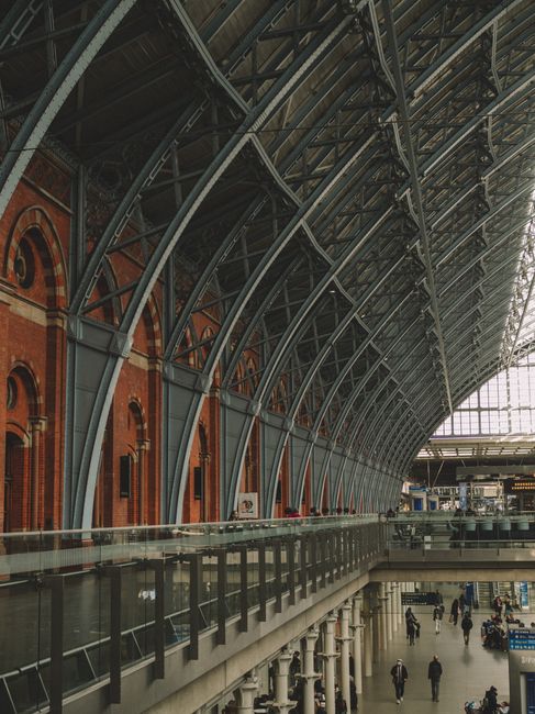The image shows the arched glass and steel ceiling of St Pancras station, with natural light streaming through the transparent panels, highlighting the intricate metal framework. At the lower part of